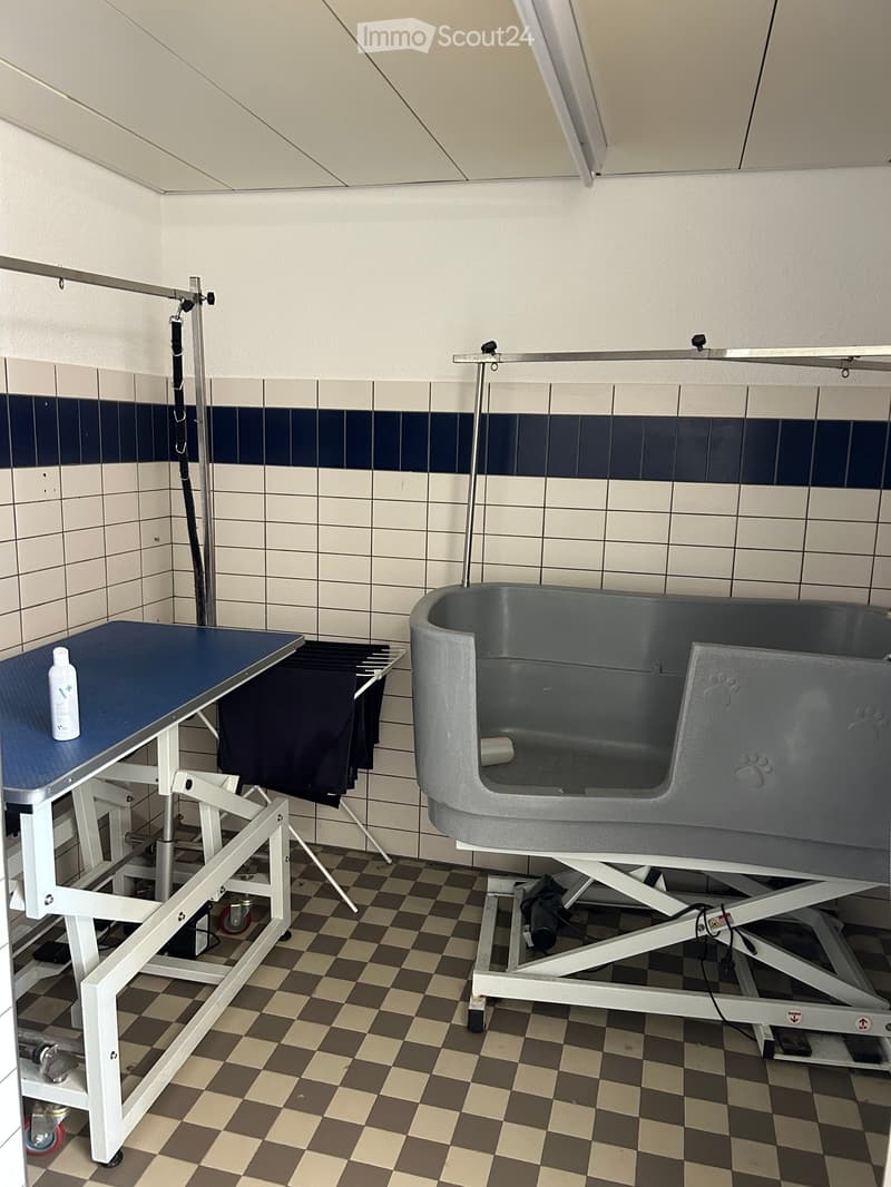 A pet grooming area with a raised table, a bathtub, and a bottle of pet shampoo on the table.