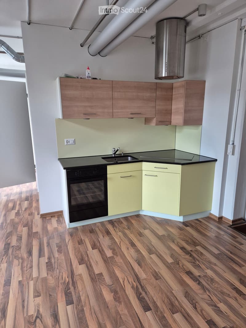 Modern kitchen with wooden cabinets, light green lower units, black countertop, and stainless steel sink and faucet. Wooden flooring throughout.