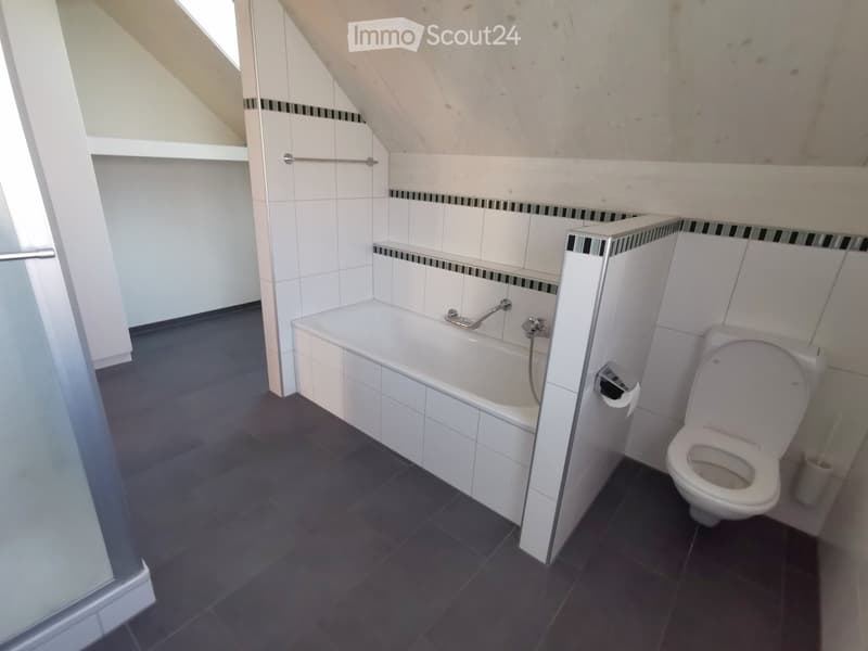 Modern bathroom with a bathtub, toilet, and glass shower enclosure. The walls are tiled with white tiles and black accents, and the floor is dark tiled.