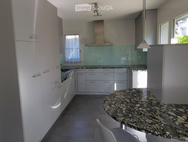 Modern kitchen with white cabinets, stainless steel appliances, a central island with a stone countertop, and a hanging light fixture.