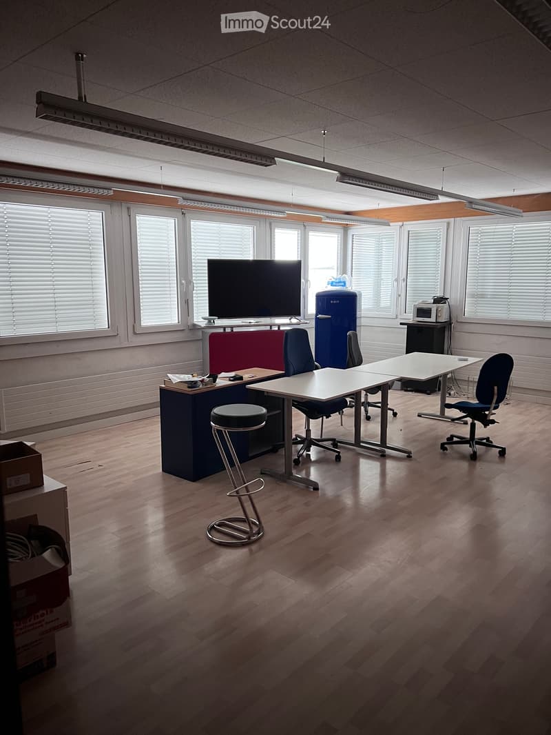 Large empty office with light wooden floors, fluorescent lighting, and multiple desks and chairs, with various electronics.