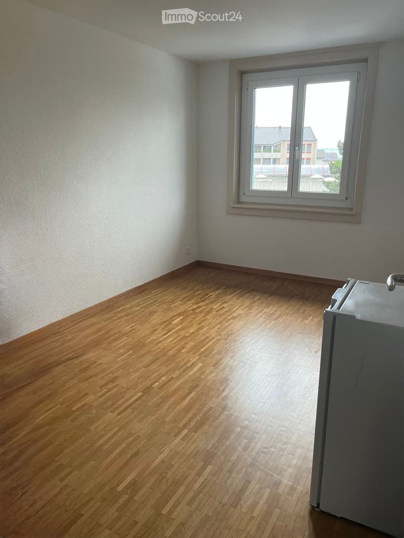 Empty room with wooden flooring and white walls, featuring a large window with a view of the outside.