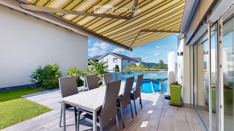 A covered outdoor patio with a dining table and chairs, a swimming pool, and a view of the surrounding landscape.