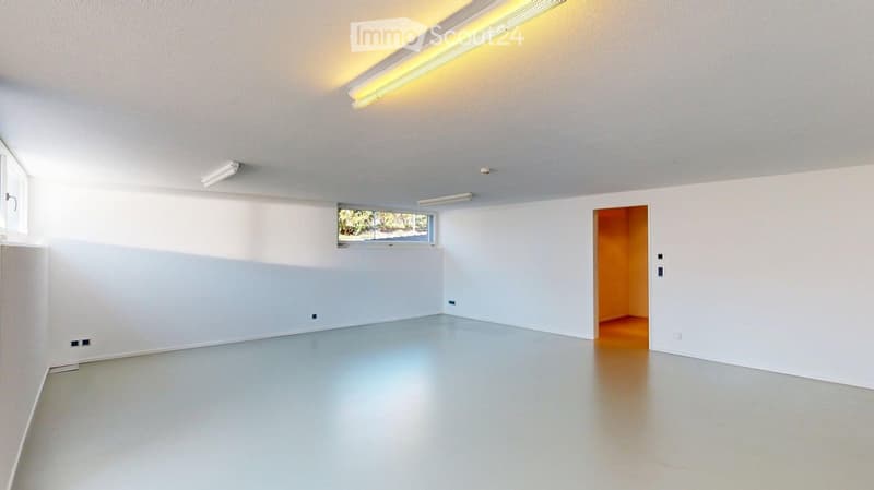 Empty room with white walls, a large window, and a door leading to another space. The floor is smooth and light-colored, and the ceiling has fluorescent lighting.