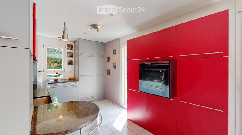 Modern kitchen with red and grey cabinets, a central island with a granite countertop, built-in oven, and pendant lighting.