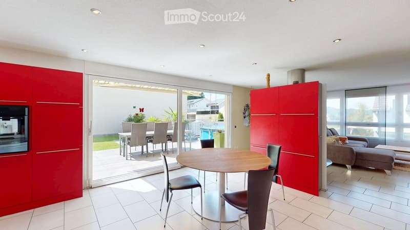 Modern open-plan living and dining area with red cabinets, a round dining table, sofa, and large sliding glass doors leading to a patio.