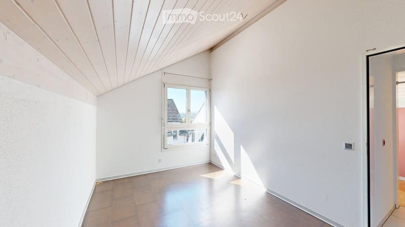 Empty room with white walls, wooden ceiling, tiled floor, and a window showing a view of a roof. No furniture or equipment present.