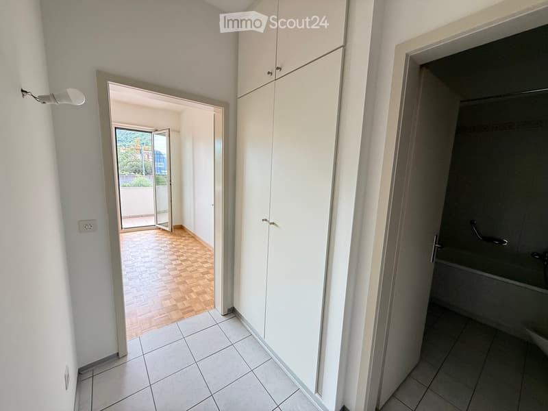 Empty hallway with white walls, tiled floor, built-in white cabinets, and an open door leading to a balcony area with wooden flooring.