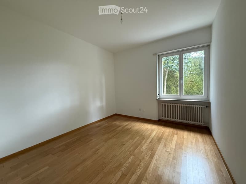 Empty room with wooden flooring, white walls, and a large window with a radiator below it.