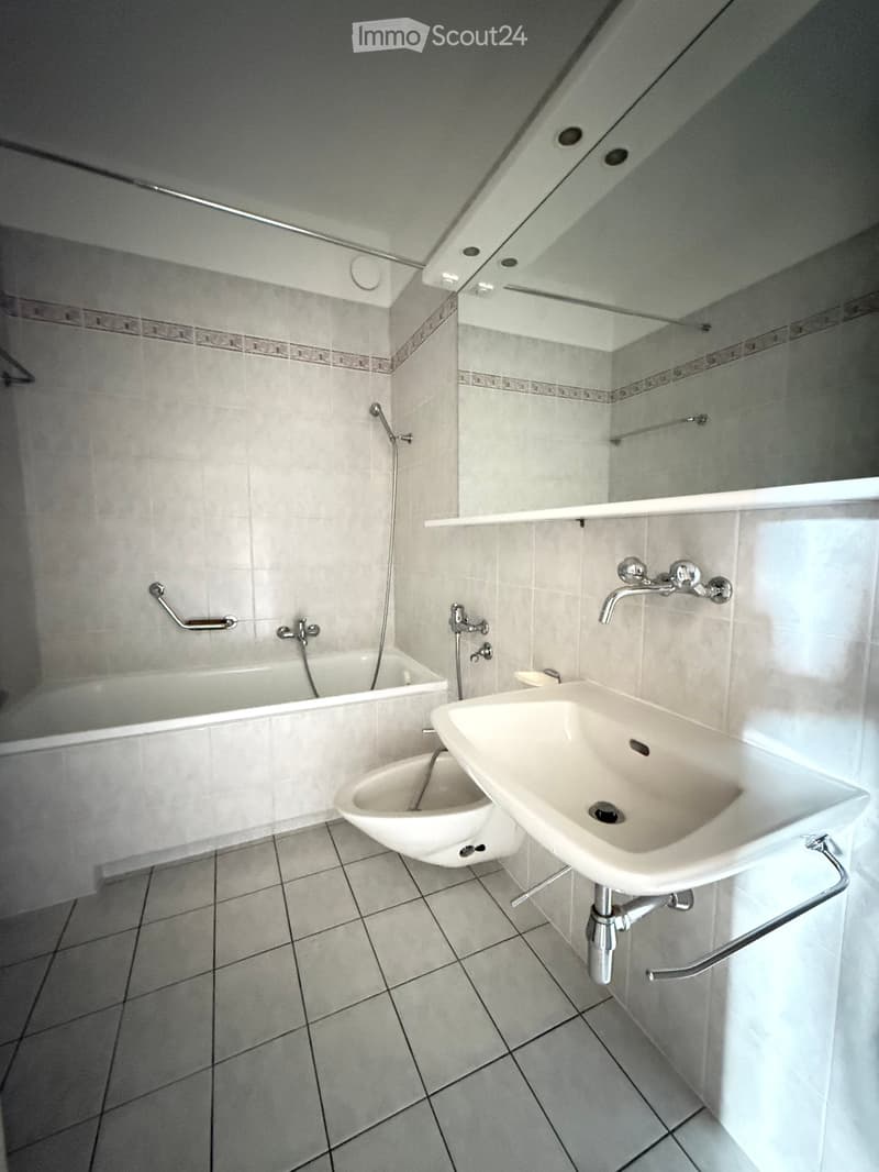 Modern bathroom with a bathtub, sink, toilet, and a large mirror above the sink.