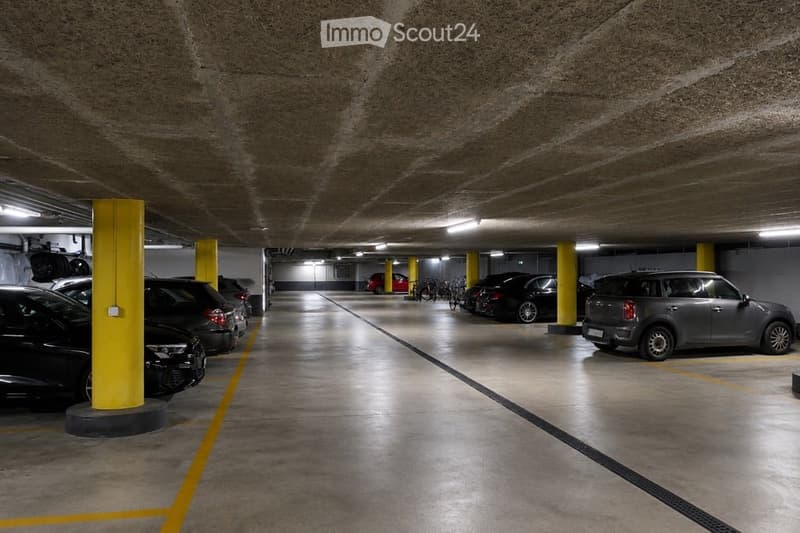 Underground parking area with several parked cars, yellow pillars, and marked parking spaces.