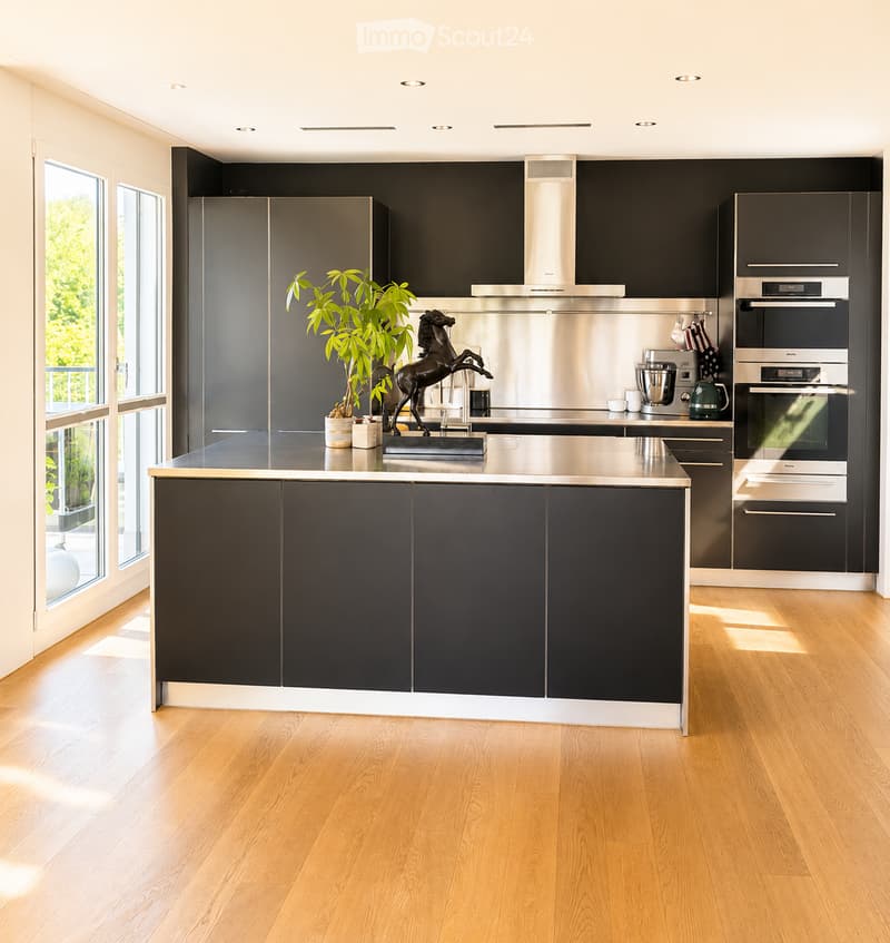 Modern kitchen with dark grey cabinets, stainless steel appliances, island, and large windows letting in natural light.