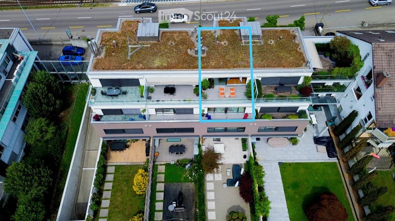 Aerial view of a modern multi-story residential building with balconies, outdoor seating areas, and surrounding greenery.
