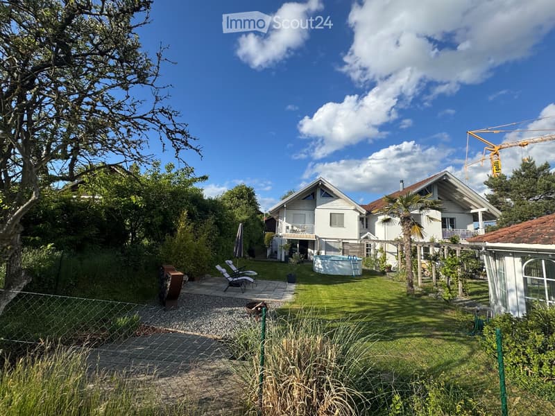 A well-maintained garden with a swimming pool, lounge chairs, a pergola, and a modern house in the background.