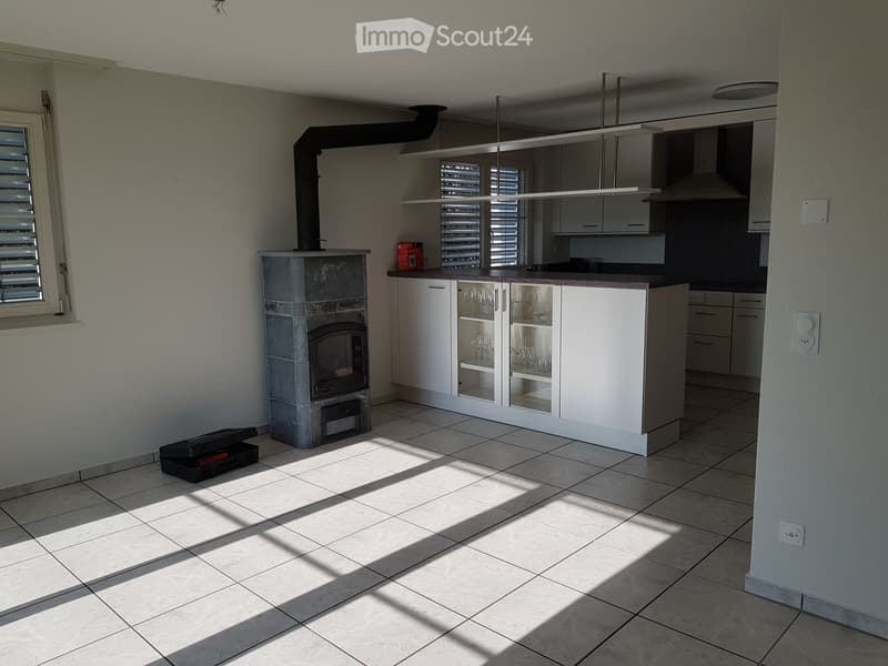 Bright, modern kitchen with white cabinets, a central island, a fireplace, and a wine rack. Sunlight streams in from a window, casting shadows on the tiled floor.
