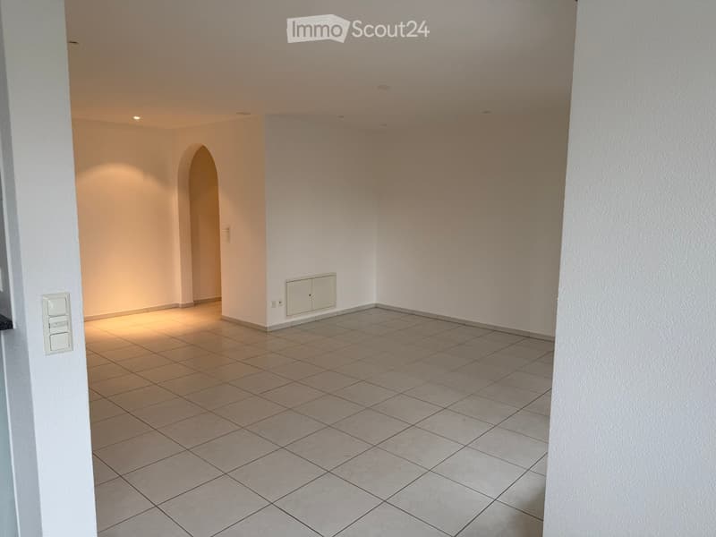 Empty room with tiled floor and white walls, featuring recessed lighting and an arched doorway leading to another space.