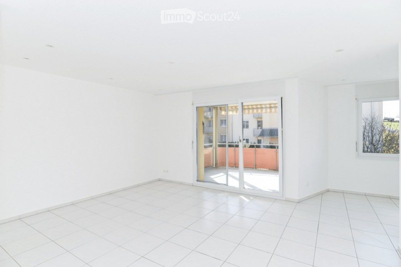 Empty room with white tiled flooring, white walls, and large sliding glass doors leading to a balcony area.
