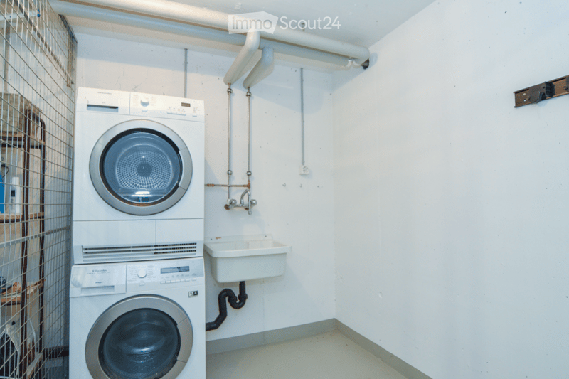 Compact bathroom with stacked washing machine and dryer, a small sink, and white tiled walls.