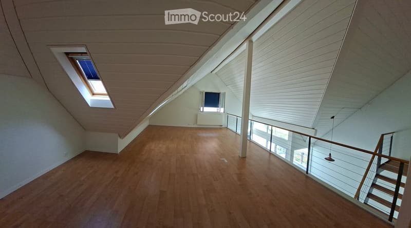 Bright, empty attic space with wooden flooring, slanted ceilings, and skylights. Features a modern glass staircase leading to another level.