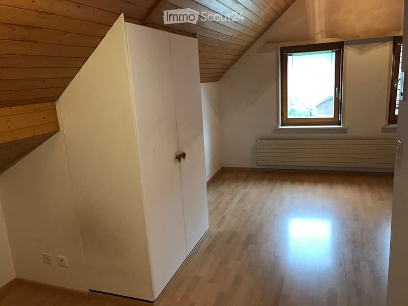 Empty room with wooden flooring, white walls, and a large window letting in natural light. Features a built-in closet and a radiator under the window.