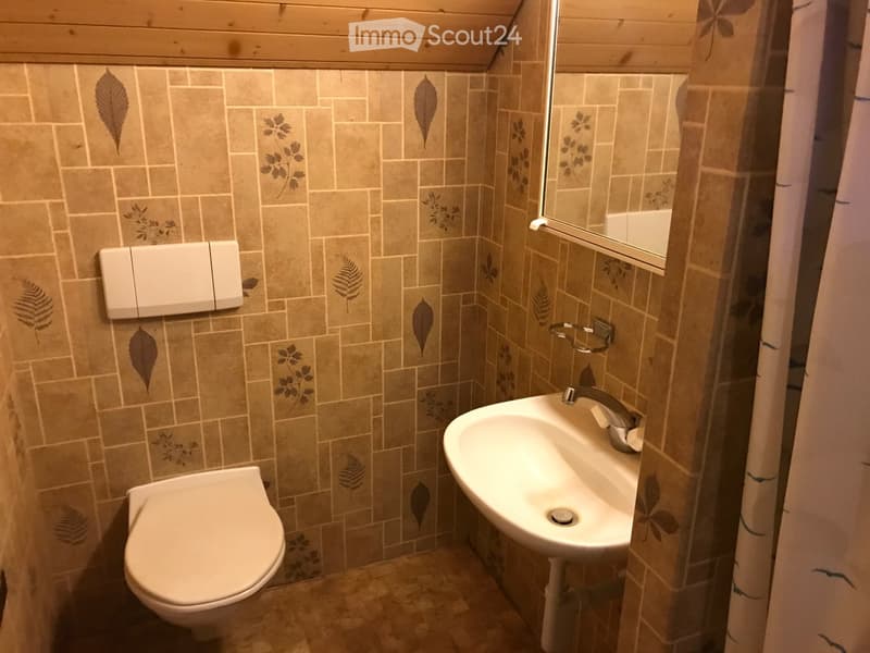 Small bathroom with beige tiled walls featuring leaf designs, a toilet, a sink with a modern faucet, and a mirror above the sink.