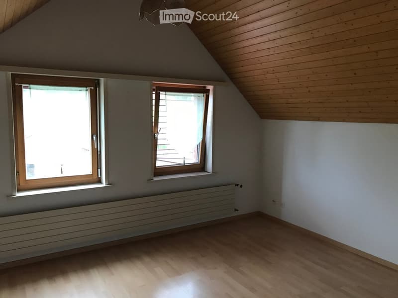 Empty attic room with wooden floors, white walls, two windows, and a radiator under one window.