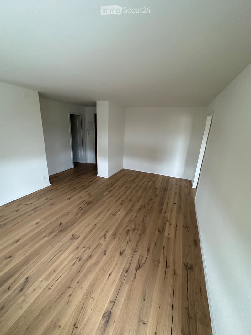 Empty room with light wooden flooring and white walls, featuring a doorway leading to another room.