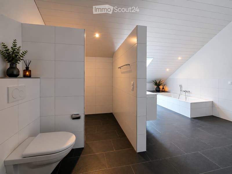 Modern bathroom with white tiles, dark floor, toilet, bathtub, and decorative plants on shelves.