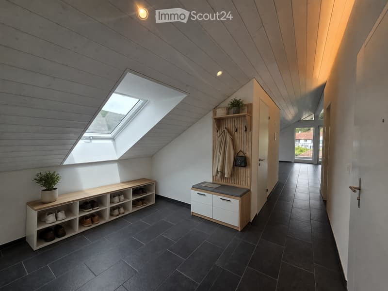 Modern hallway with dark tiled floor, wooden ceiling beams, built-in shoe rack, coat rack, and bench. Skylight provides natural light.