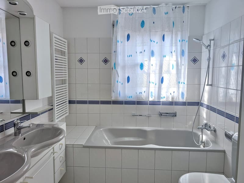 Bathroom with white tiles, a bathtub, a sink, a toilet, a mirror, a showerhead, and a radiator.