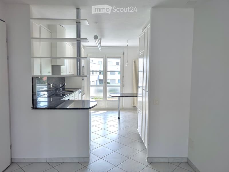 Modern kitchen with white cabinets, a black countertop, and a small dining table in the adjacent space.