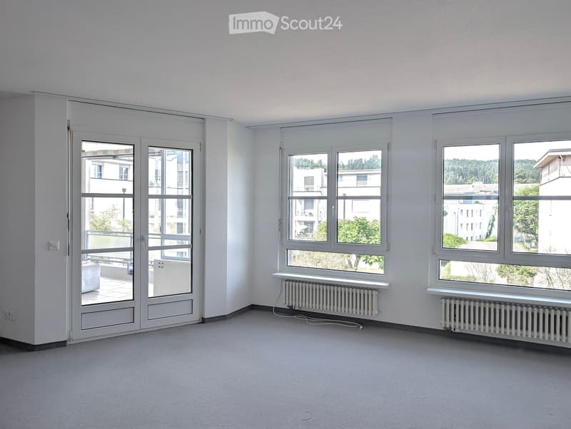 Empty room with white walls, large windows, radiators, and a sliding glass door leading to a balcony.