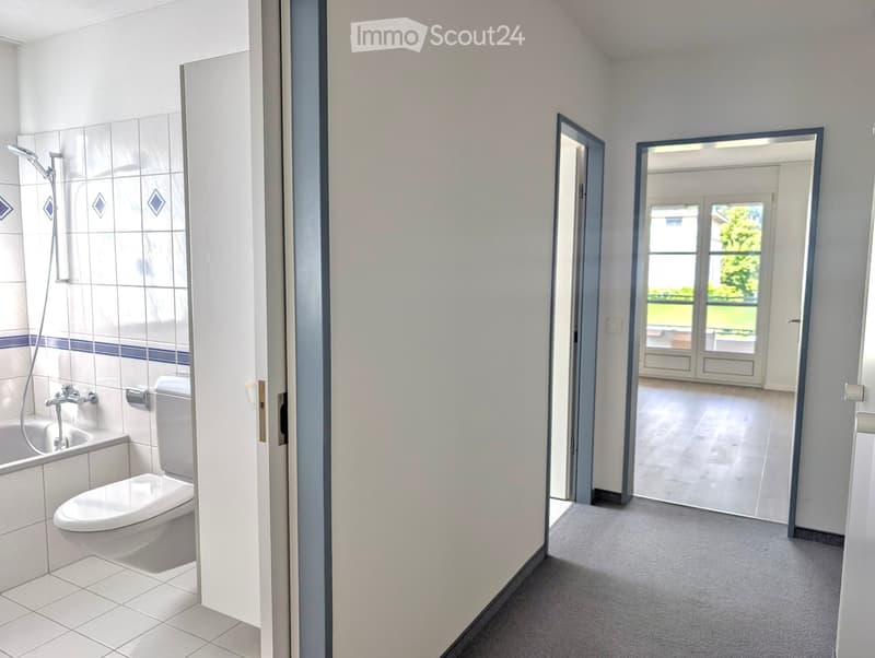 Bathroom with a toilet, bathtub, and showerhead. The bathroom has tiled walls and a door leading to a hallway.