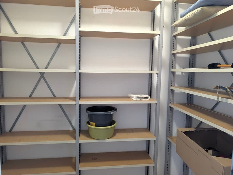 Empty storage shelves with minimal items, including a small towel, a grey bucket, and a green container.