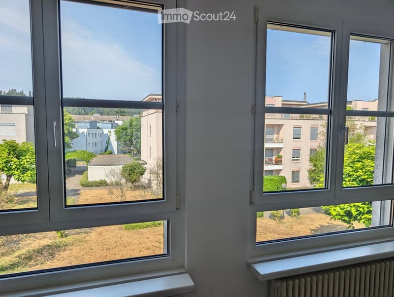View from a window showing a residential area with buildings, trees, and a clear blue sky.
