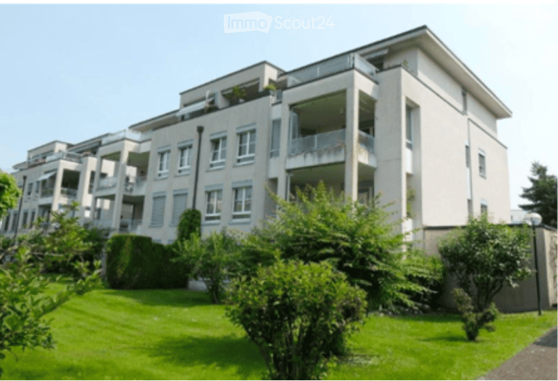 Modern multi-story apartment building with balconies, white facade, and well-maintained green lawn in front.