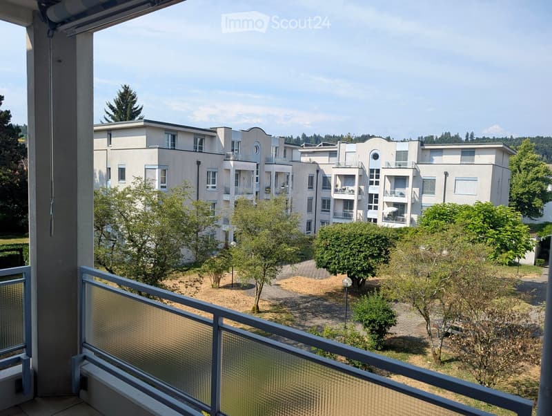 Balcony overlooking a residential complex with modern apartment buildings, greenery, and pathways.