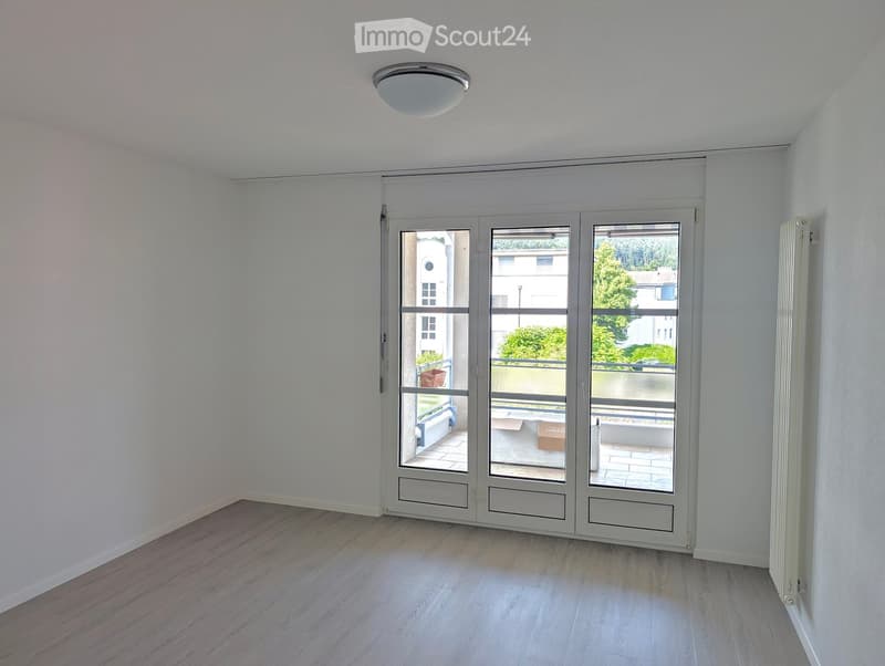 Empty room with white walls, wooden flooring, and large sliding glass doors leading to a balcony.