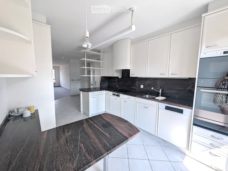 Modern kitchen with white cabinets, dark countertops, and stainless steel appliances including an oven and dishwasher. Features a central island with a dark, polished surface.