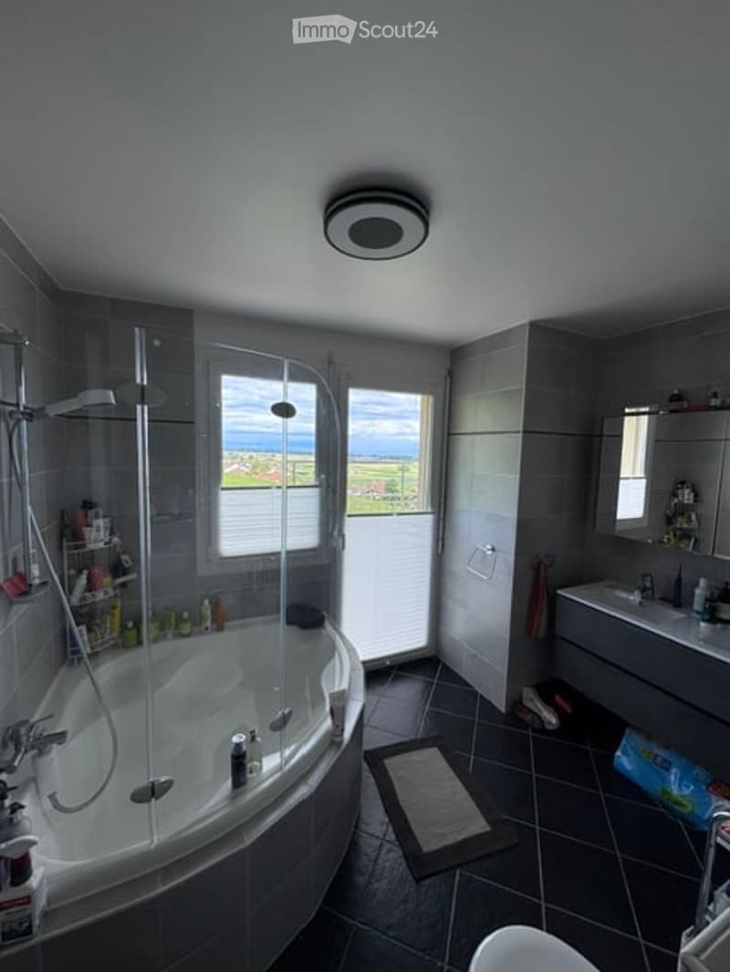 Modern bathroom with a large window offering a scenic view, featuring a bathtub, sink, mirror, shower, towel rack, and various bathroom accessories.