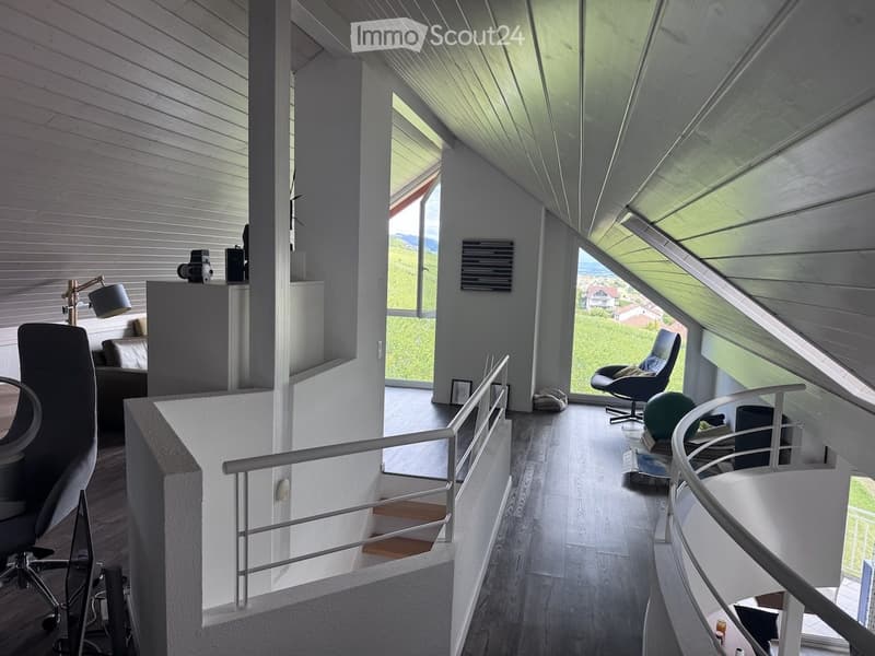 Modern, open-concept room with wooden flooring, large windows offering a scenic view, and contemporary furniture including a chair, table, lamp, cabinet, and sofa.