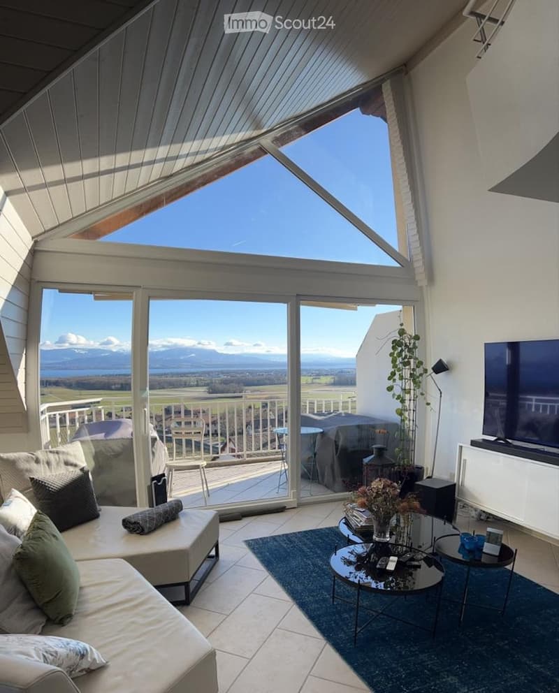 Bright living room with large windows and a view, featuring a sofa, coffee table, and television.