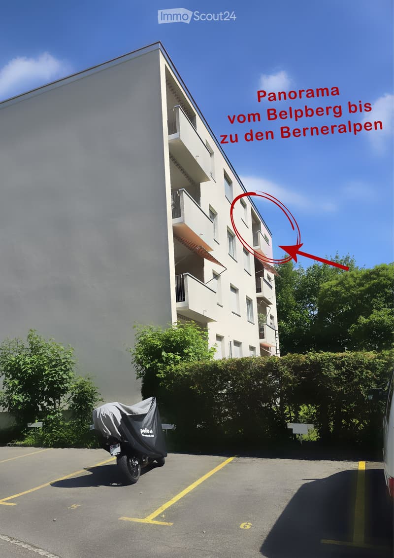 Modern multi-story apartment building with balconies, surrounded by greenery and a parking area with a covered motorcycle.