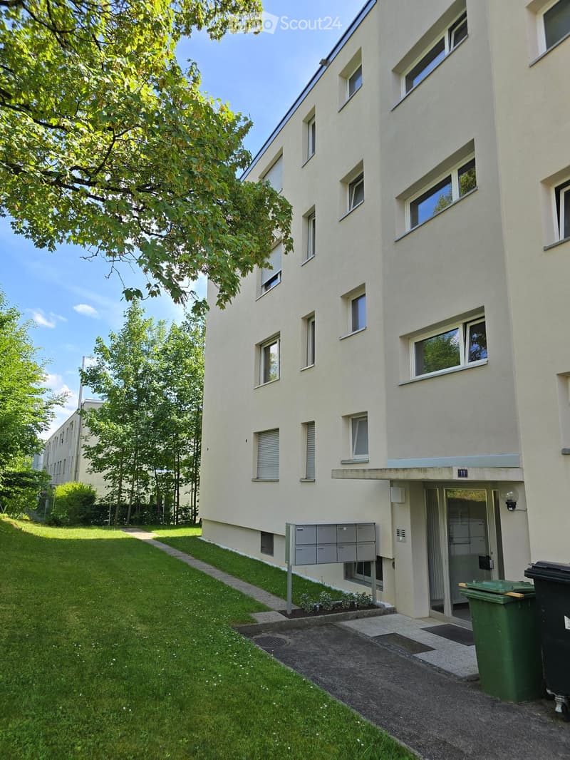 Four-story residential building with light-colored facade, multiple windows, and a small garden area in front.