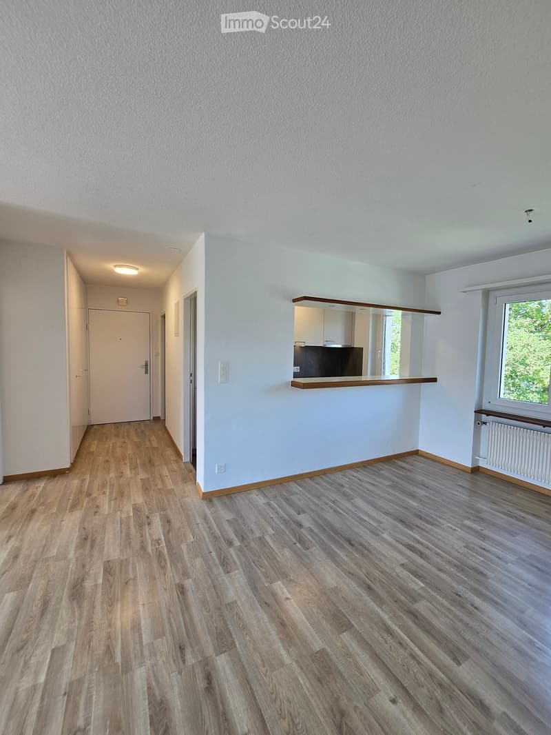 Empty hallway with wooden flooring, white walls, and a small open area with a window and a built-in shelf. No furniture or equipment is present.
