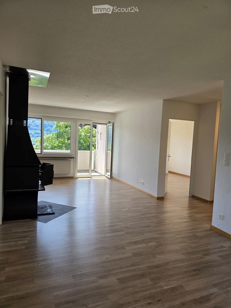 Empty room with wooden flooring, white walls, large windows, and a sliding glass door leading to a balcony.