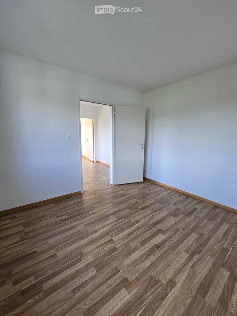 Empty room with light blue walls and wooden flooring, featuring a doorway leading to another room.