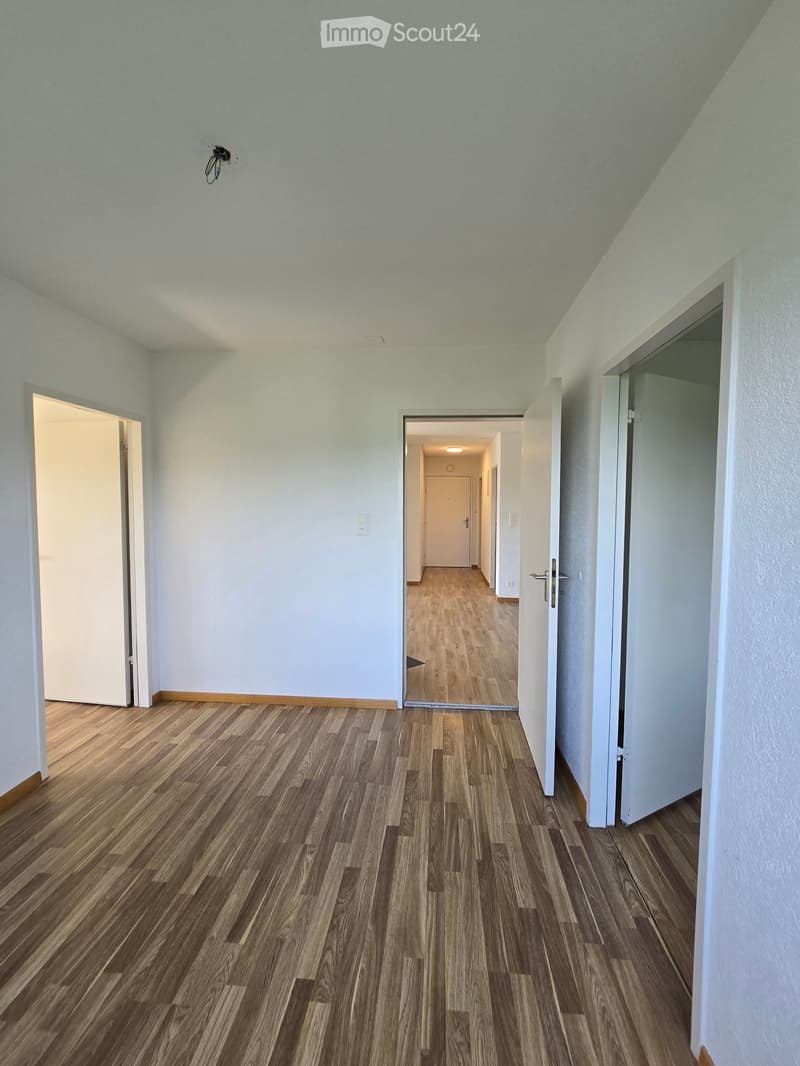 Empty hallway with wooden flooring, white walls, and multiple open doors leading to other rooms.