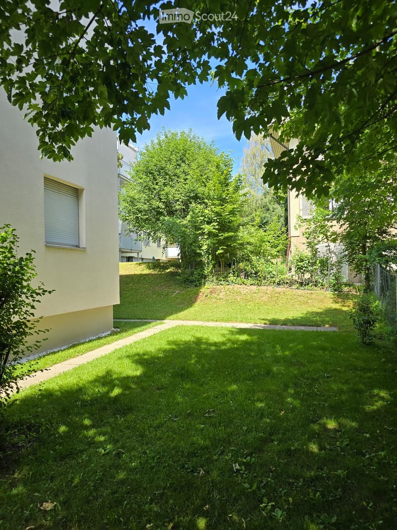 A well-maintained garden with a grassy lawn, trees, and a pathway leading to a raised section of the property.