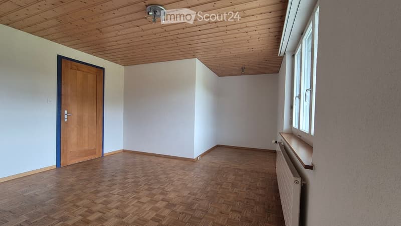 Empty room with wooden floor, white walls, and a wooden door. Natural light from windows on the right side.